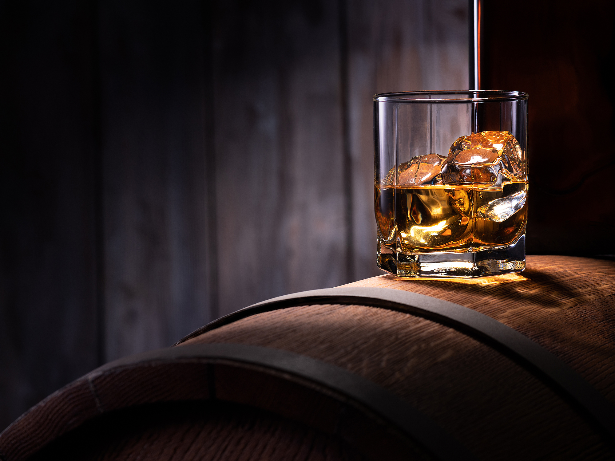 Glass of whiskey with ice cubes on the wooden barrel with wooden background